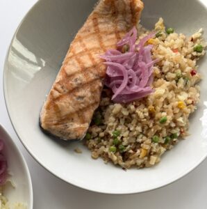 A bowl with salmon, rice, and pickled onion.
