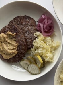 A bowl with a burger patty, cabbage, and pickled onion.