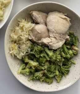 A bowl with chicken, sauerkraut, and roasted broccoli.