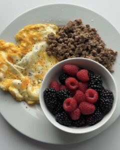 Eggs with ground beef, bowl of raspberries and blackberries.