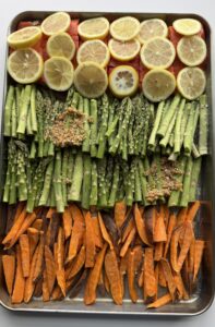 Asparagus, sweet potatoes, and sliced lemons arranged side by side on top of salmon.