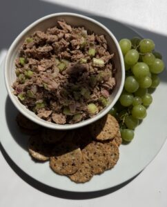 A plate with a bowl of tuna, crackers, and grapes.