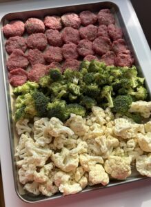 A sheet pan of raw slider patties with broccoli and cauliflower.
