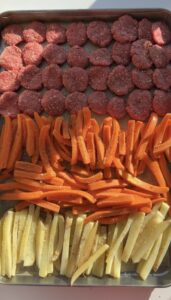 A sheet pan of raw burger patties with parsnip fries and carrots.