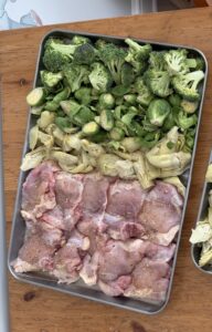 A sheet pan of raw chicken and steak with zucchini and green beans.